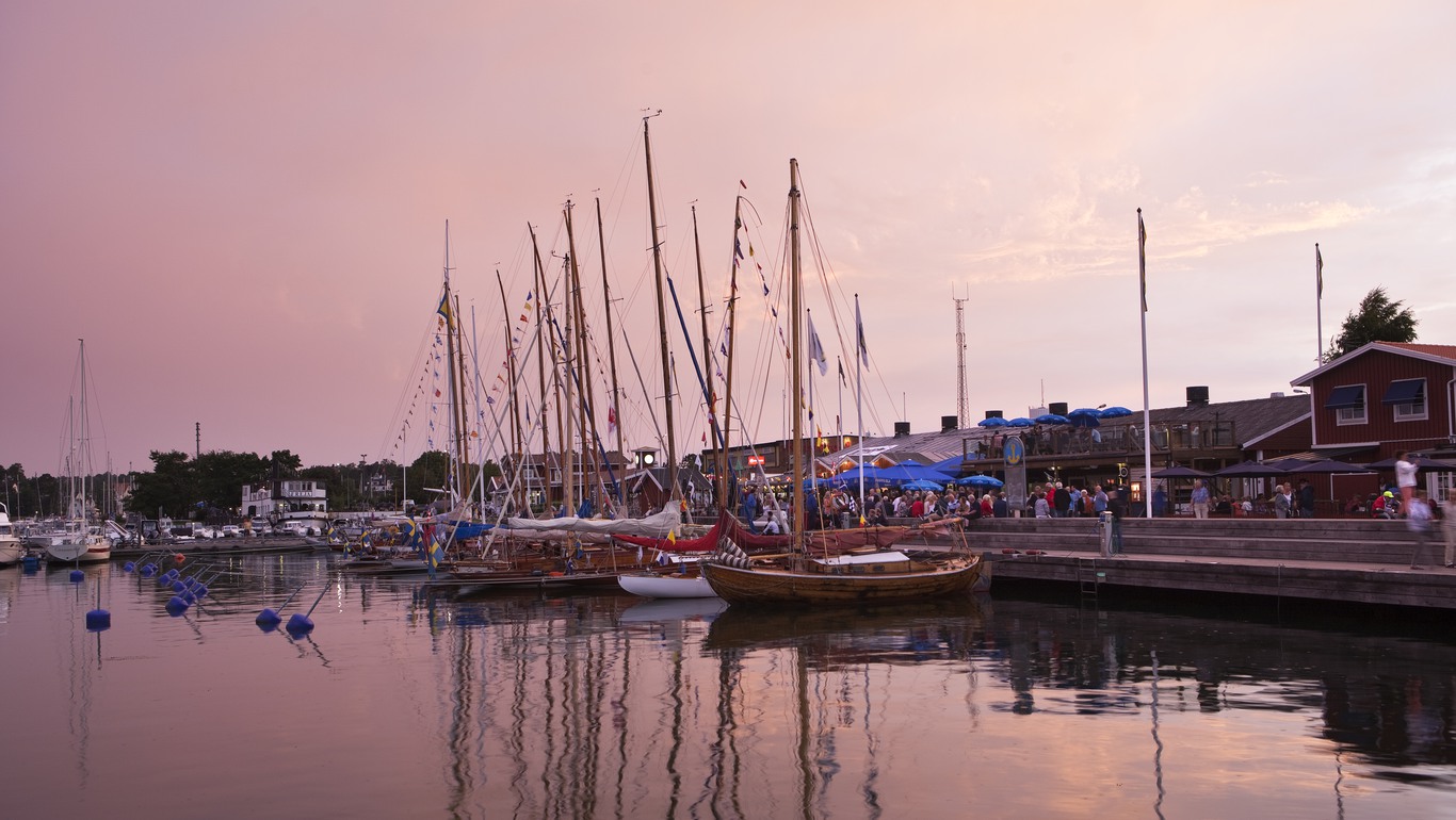 Segelbåtar och folkliv i gästhamn en vacker kväll med rosa himmel.