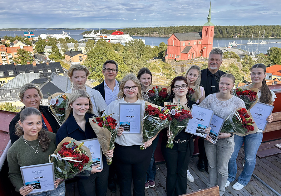 Tolv personer på balkong högt upp med utsikt mot havet bakom dem.