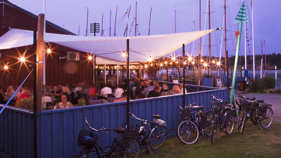 Uteservering med parkerade cyklar utanför i Nynäshamns fiskehamn en sommarkväll.