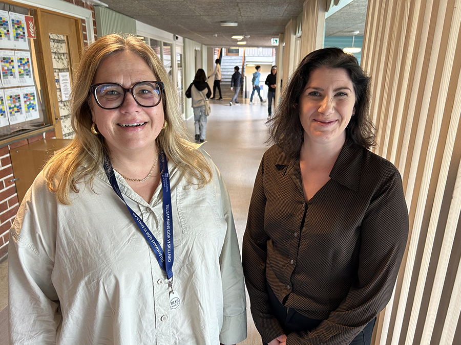 Två kvinnor i skolkorridor. Elever syns i bakgrunden.