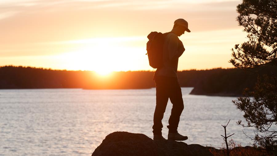 Man vandrar på klippa vid havet i solnedgång.